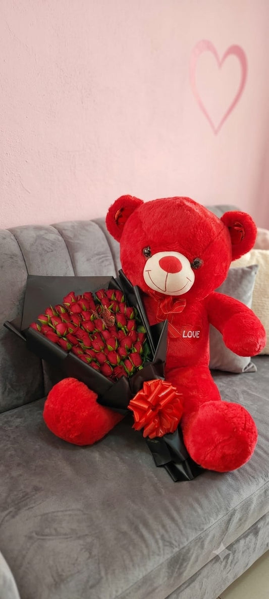Giant red plush LOVE teddy bear with red roses bouquet in black wrap and red satin bow on grey sofa with heart on pink wall